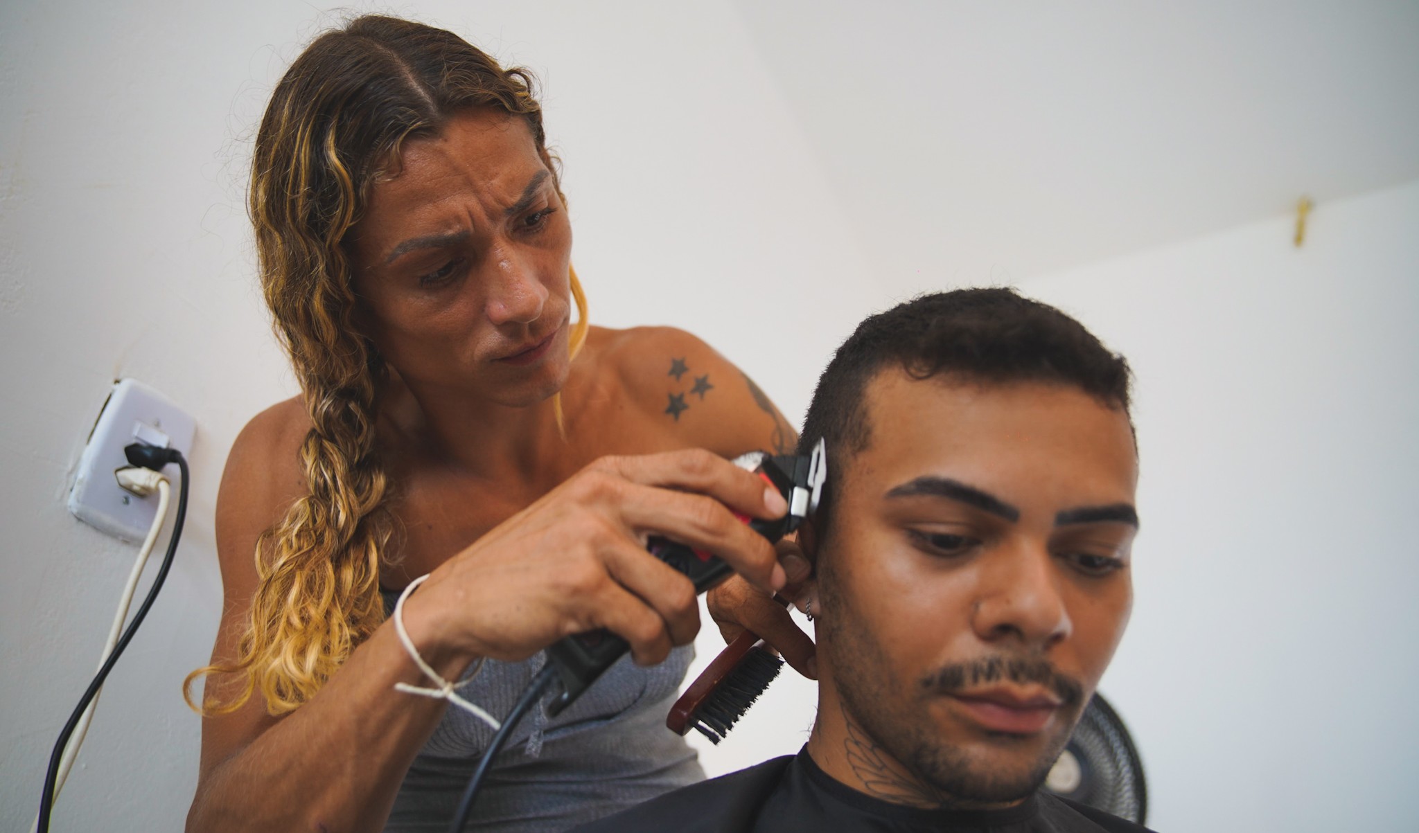 Letícia Marques corta o cabelo de um rapaz durante a aula do curso de corte de cabelo masculino